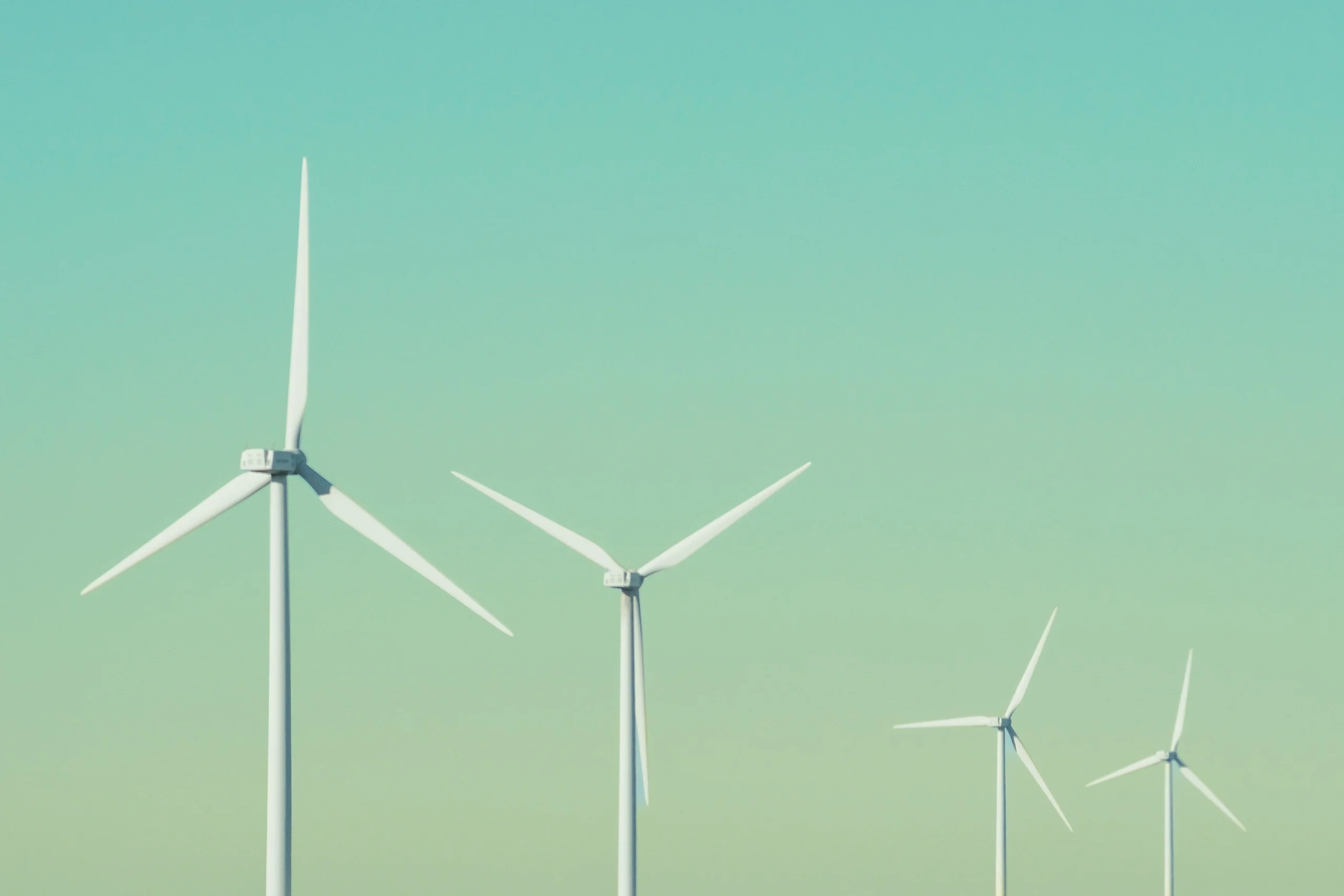 Witte windturbines met lange wieken verspreid over de horizon tegen een blauwe en groene lucht.