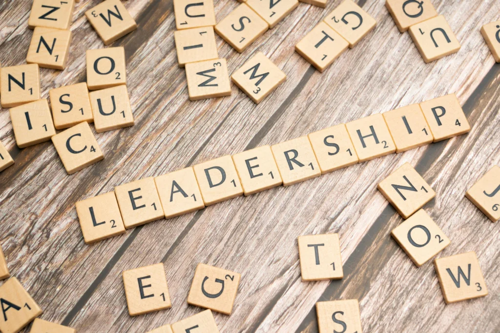 Houten tafel met scrabble-tegels waarop het woord leadership centraal gevormd is.